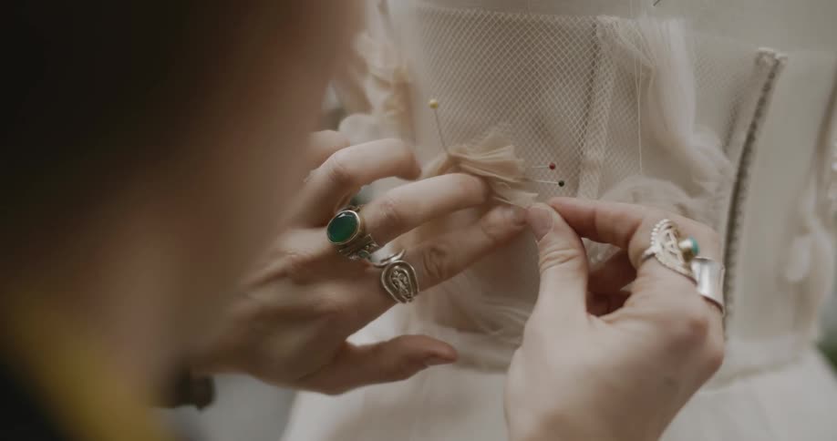 Closeup of a womans hands sewing the back of a dress with needles