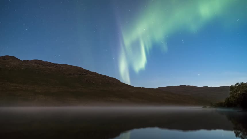 Landscape of a reflective lake next to a mountain with the sky on electric timer in northern lights