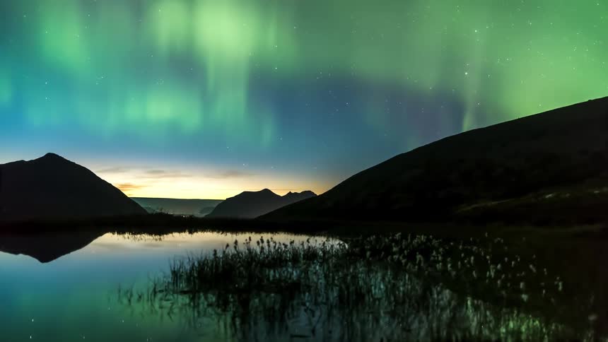The northern lights reflecting their green beams in the water of a lake at night
