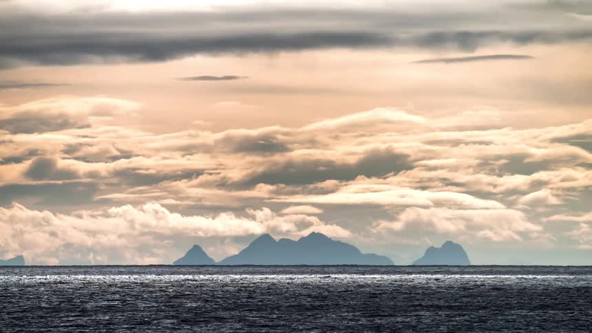 Boat silhouetted against foggy coastal mountains crosses ocean under a red tinted sky