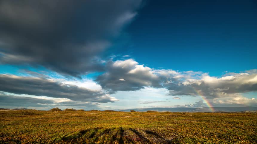 A rural region with a large field of grass and clouds passing in the sky to the left