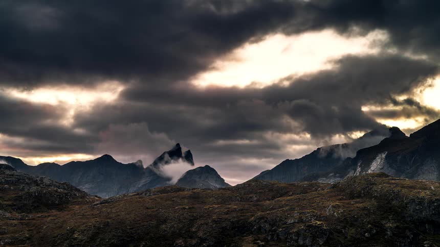 Landscape of a reddish sky with black clouds over mountain ranges