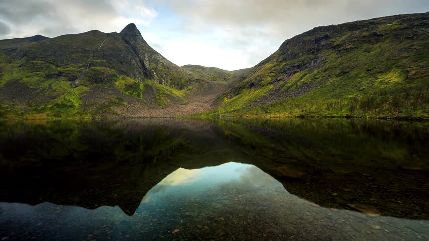 A still water of a lake reflecting the surrounding environment which is full of mountains and low vegetation