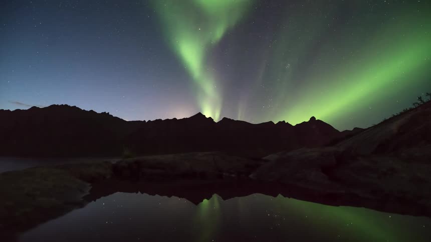 Landscape at night of the aurora borealis reflecting in a lake amidst mountains at night