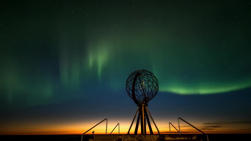 A metallic and circular object is pointed towards the sky where there is a green aurora borealis on a morning