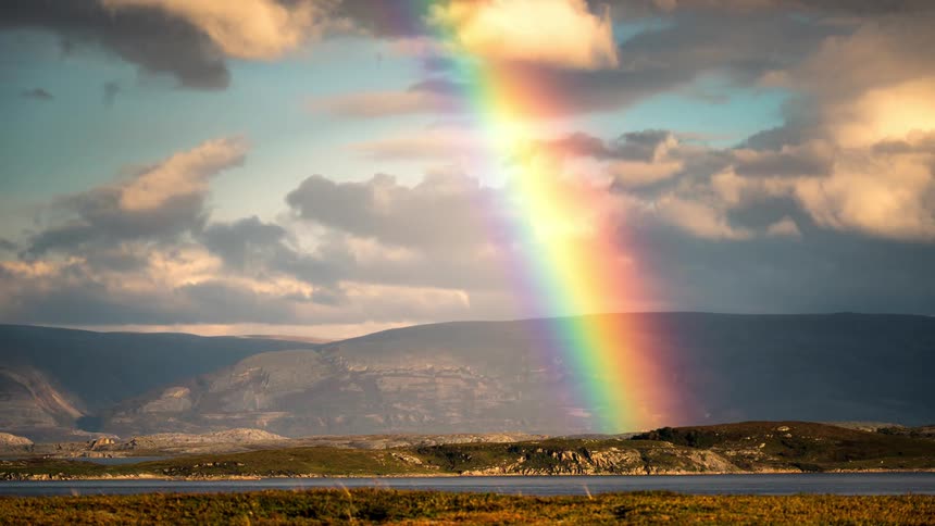 Natural landscape with a side and mountains and a huge rainbow disappearing in time lapse