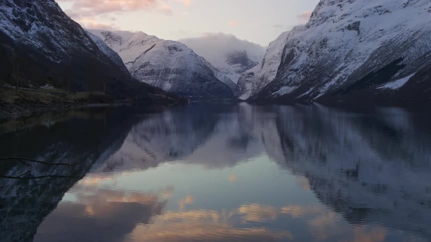 A lake in a mountainous region that is reflecting the mountains that are covered with snow