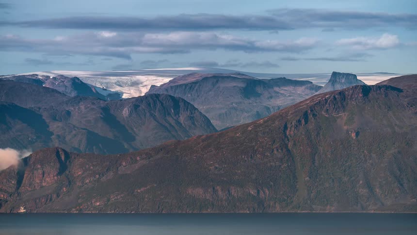 A region with many mountains and several clouds in the sky moving to the right