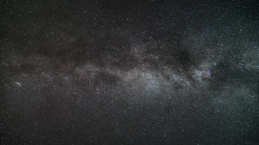 A huge night sky is scattered with many tiny stars around a galaxy