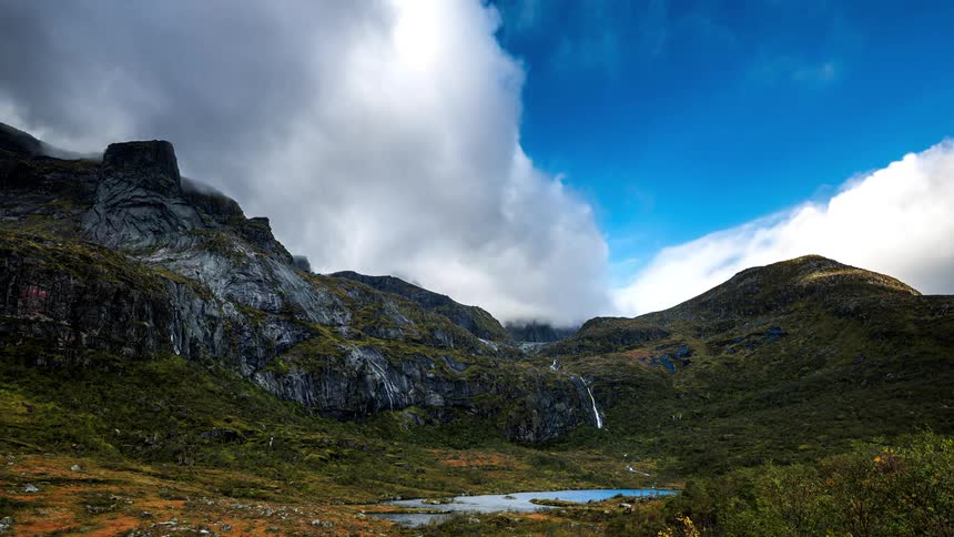 Clouds passing quickly in the sky near a mountain with a vase and lots of vegetation