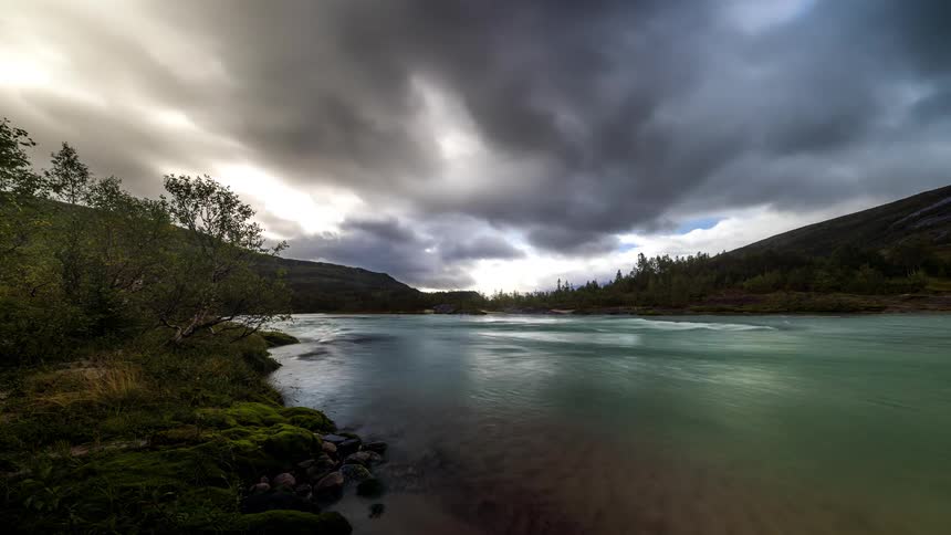 A shore on one side where many waves are arriving and the clouds in the sky are dark