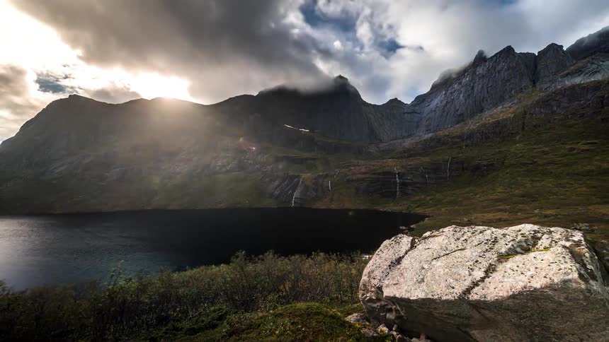 Landscape of mountains with vegetation and a central lake with clouds passing by in timelapse