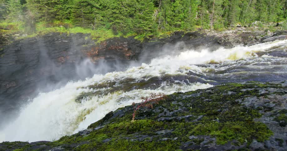 A stream that turns into a waterfall with a huge waterfall and behind it there are several trees