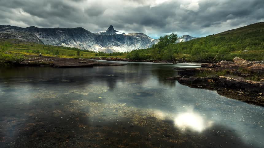 Fish swim through waters reflecting clouds passing over mountains