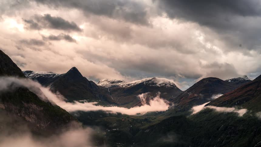 A mountainous region with several clouds passing by