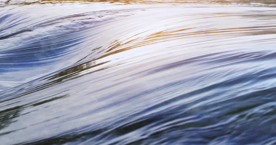 A water that is going to the left following a path with some unevenness and its surface is reflecting the sky