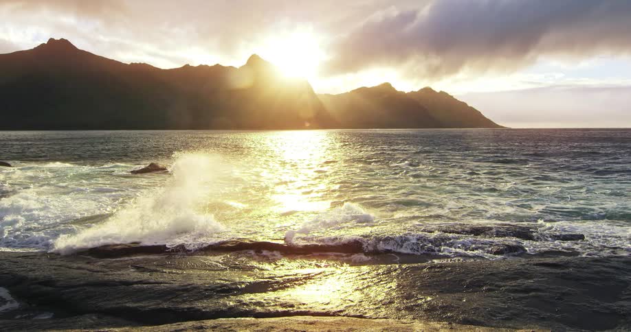 The sun sets behind the mountain range near the sea