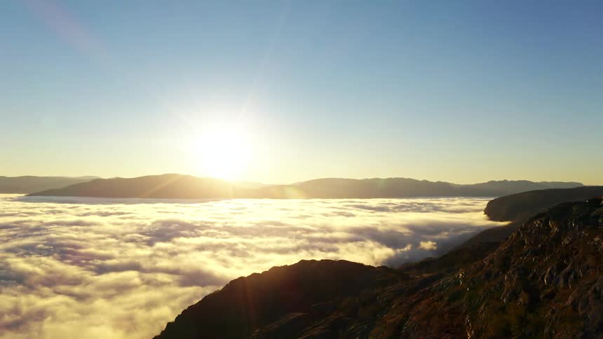Aerial panorama of the sun on the horizon with mountains above cloud level