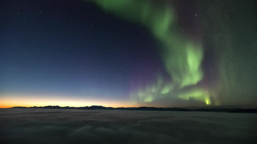 View above the clouds and overlooking the sky of the northern lights and silhouette of mountains