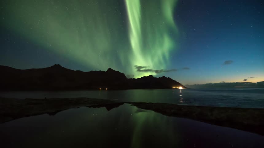 The aurora shines green over the mountains