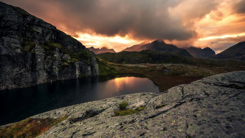 Clouds float over a lake and a mountainous area at sunset