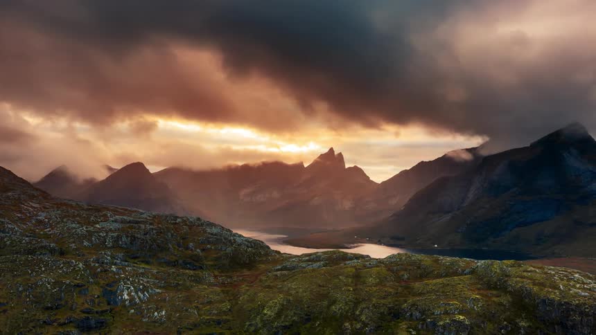 A landscape of mountains being illuminated by the sun and a lake in the middle of them