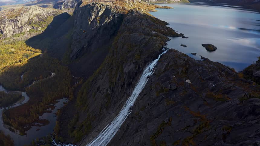 Aerial panorama of a lake giving access to a waterfall in a natural environment with ruined forests and mountains