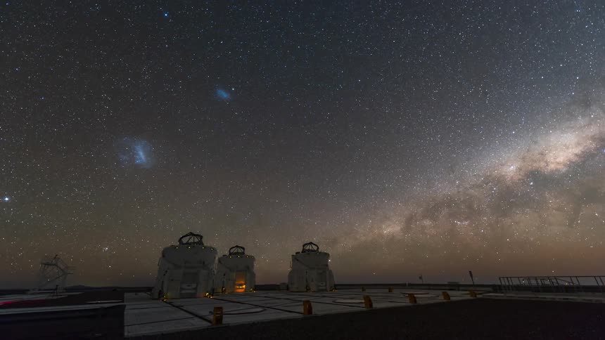 A galaxy is visible in the night sky over an observatory
