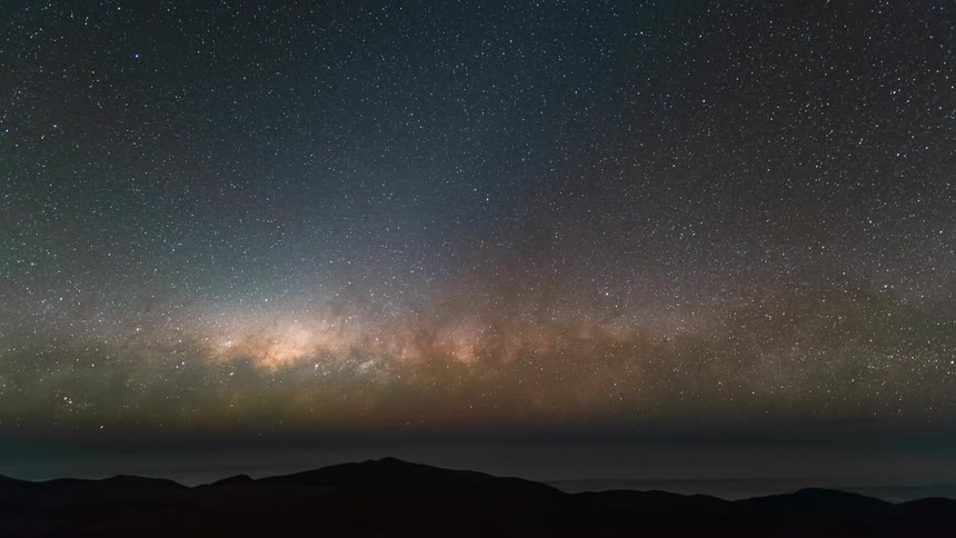 A nebula in the starry sky illuminating the mountainous desert
