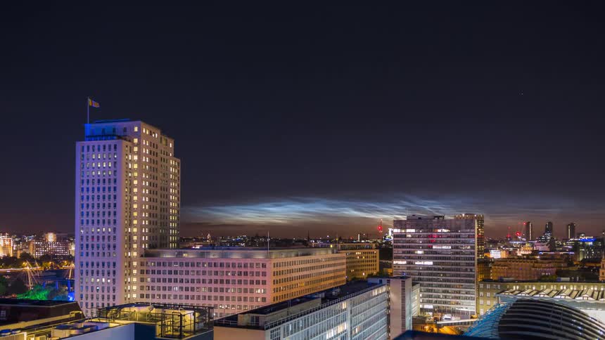 Some big commercial buildings in a city with lights on at night