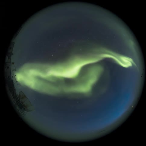 fisheye view of a research station with the Aurora Australis lighting up the starry night sky