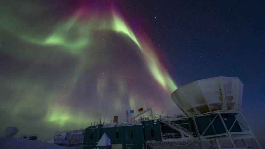 An Aurora Australis glowing green in the sky above an observatory