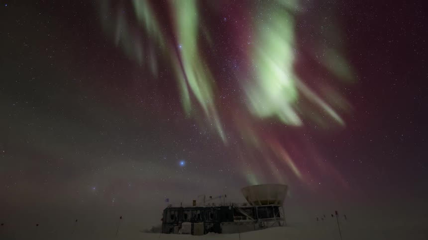 Aurora Australis over a research station and under a starry night sky