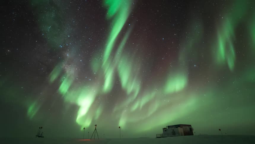 a person with a tripod at a research station with Aurora Australis overhead