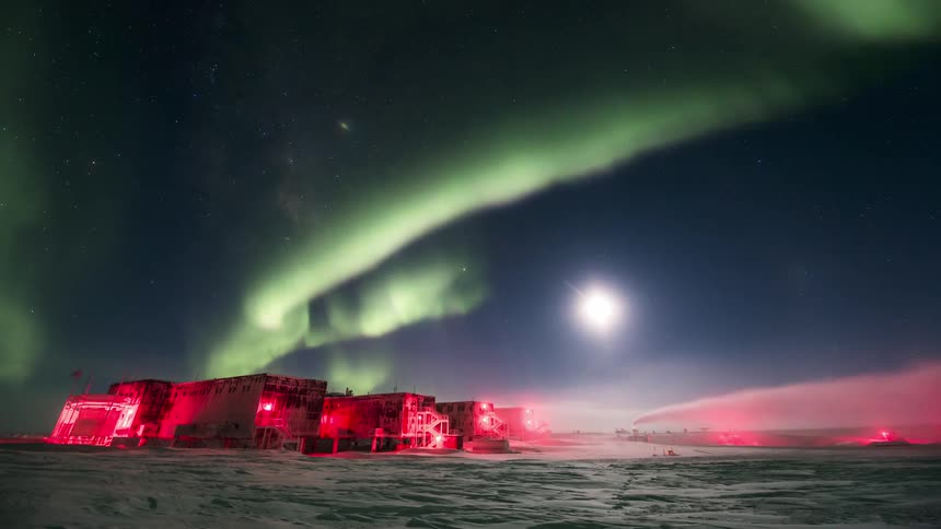 Aurora Australis shining over a research station covered in red lights