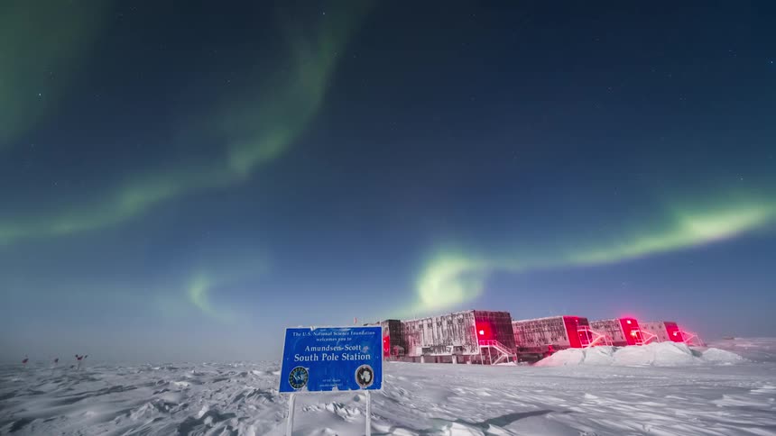 An Aurora Australis in a blue sky with a person near an observation camp and a blue sign