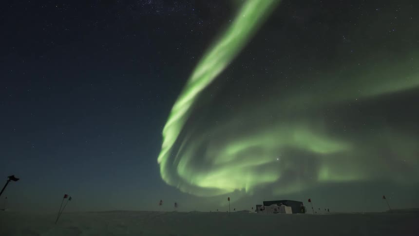 Man placing a camera on a snowcovered ground overlooking the night sky with  Aurora Australis