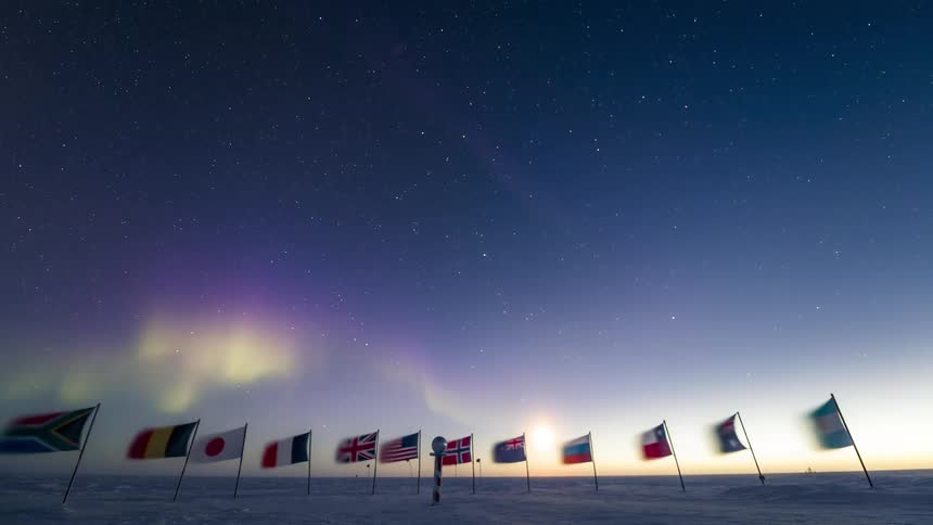 Flags of different countries at the south pole with a view of the sky in timelapse with Aurora Australis