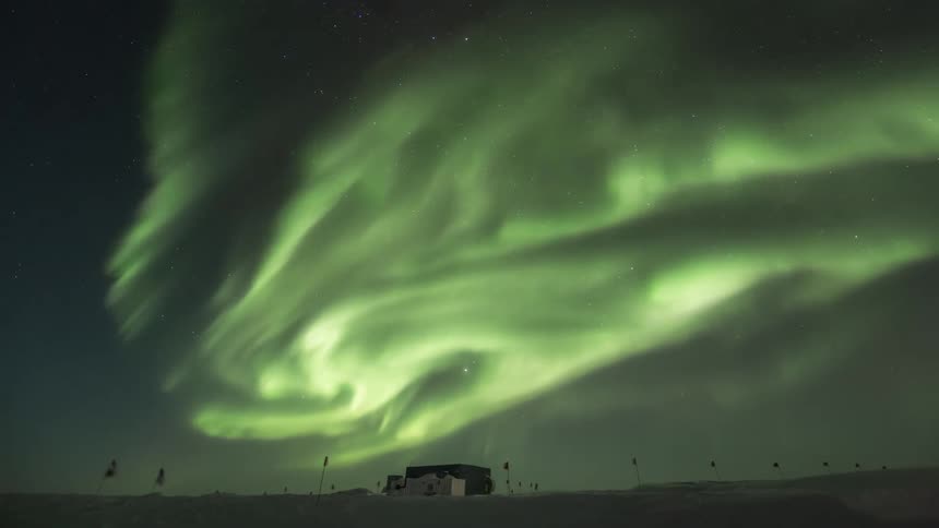 Green Aurora Australis above a small cabin in a region with many flags