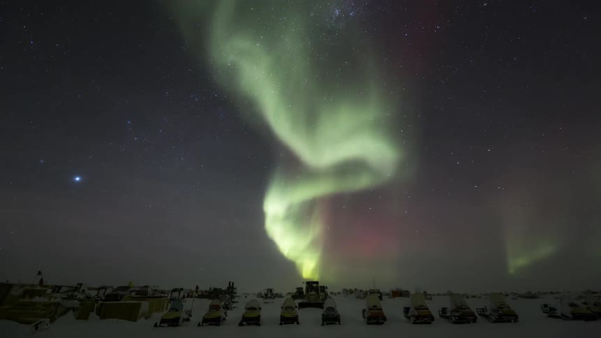 The Aurora Australis with intense green glow in the sky in antarctica with parked vehicles