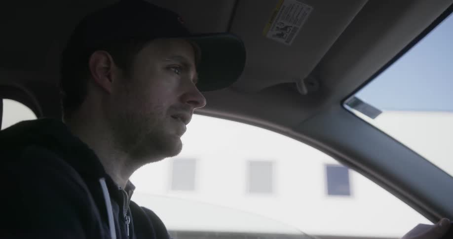 A man wearing a chicago cubs baseball cup looks around while driving