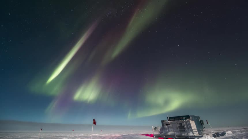 A research station in antarctica illuminated by the Aurora Australis in the starry sky
