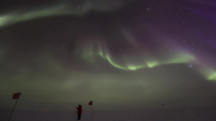 Aurora Australis over a field marked with flags with a person coming to install a device next to one of the flags