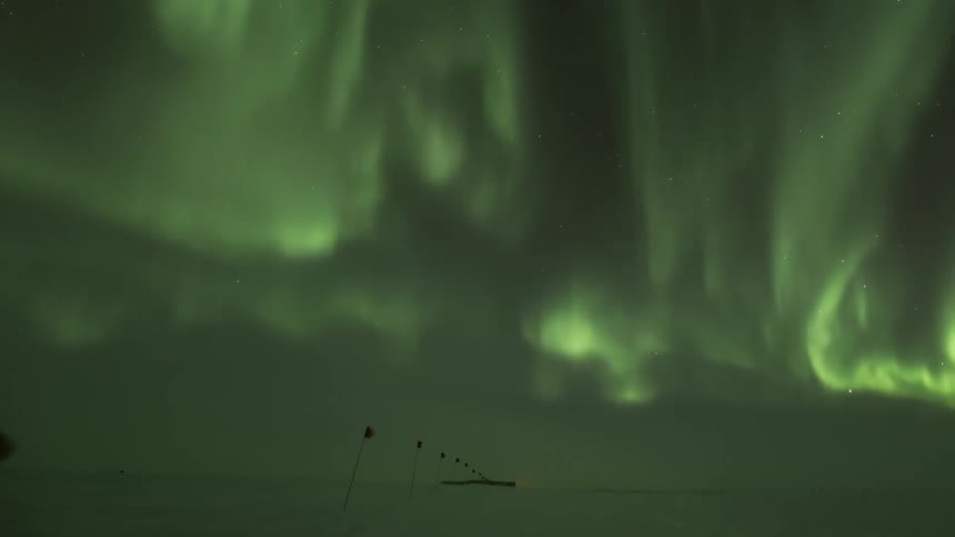 Aurora Australis shining over a snow covered ground with flag markers