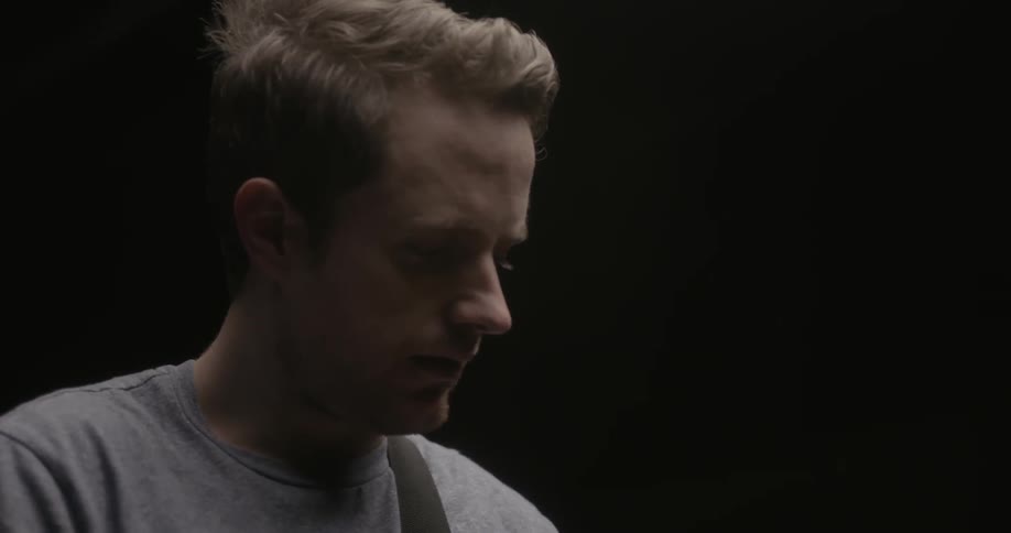 A blond man plays guitar in a dark room