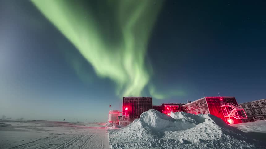 Aurora Australis shining over a research station on a snowy plain