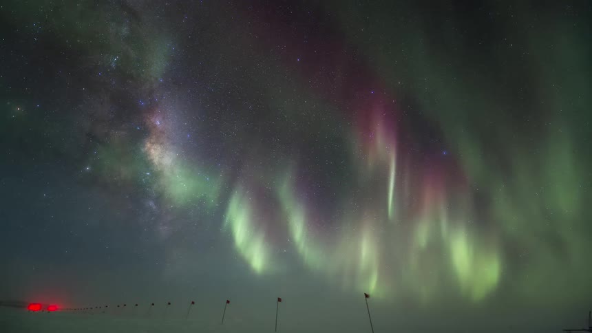A green beam of the Aurora Australis in the sky in antarctica and flags on the ground