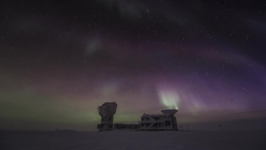 An Aurora Australis with green and pink rays on top of an observatory in antarctica