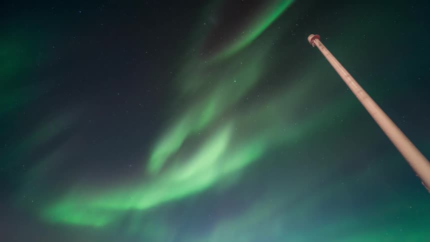 A green Aurora Australis in the sky and there is a tall post on the right side