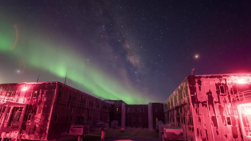 The Aurora Australis with a green glow moving in the sky in an area with some buildings